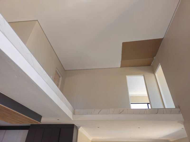 An open-plan interior space featuring a mezzanine level with marble-look trim and recessed lighting, currently showing unfinished ceiling work.