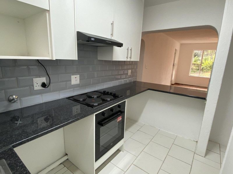 A clean, functional kitchen featuring white cabinetry, dark granite countertops, subway tile backsplash, and integrated electric oven and hob with an extractor fan.