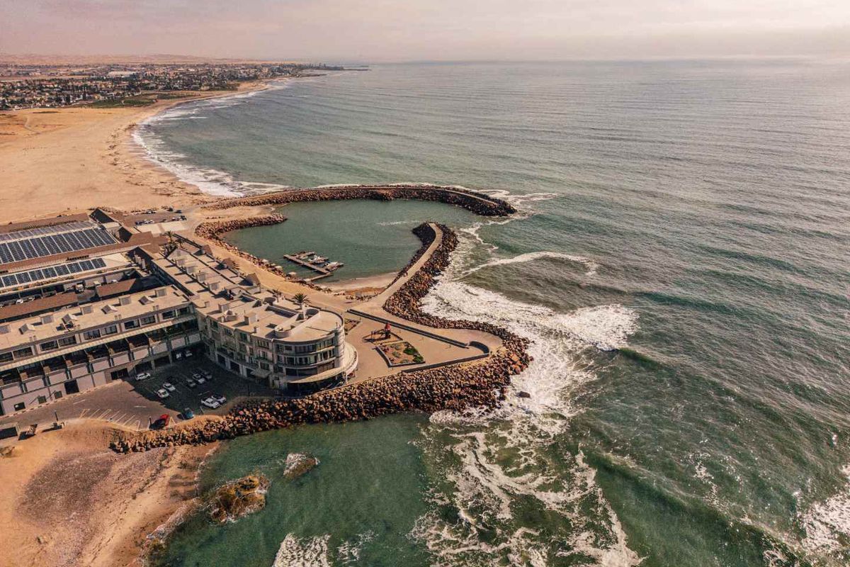 Aerial view of the apartment complex situated on the coastline, featuring solar panels, dedicated parking, and direct access to the oceanfront breakwater.