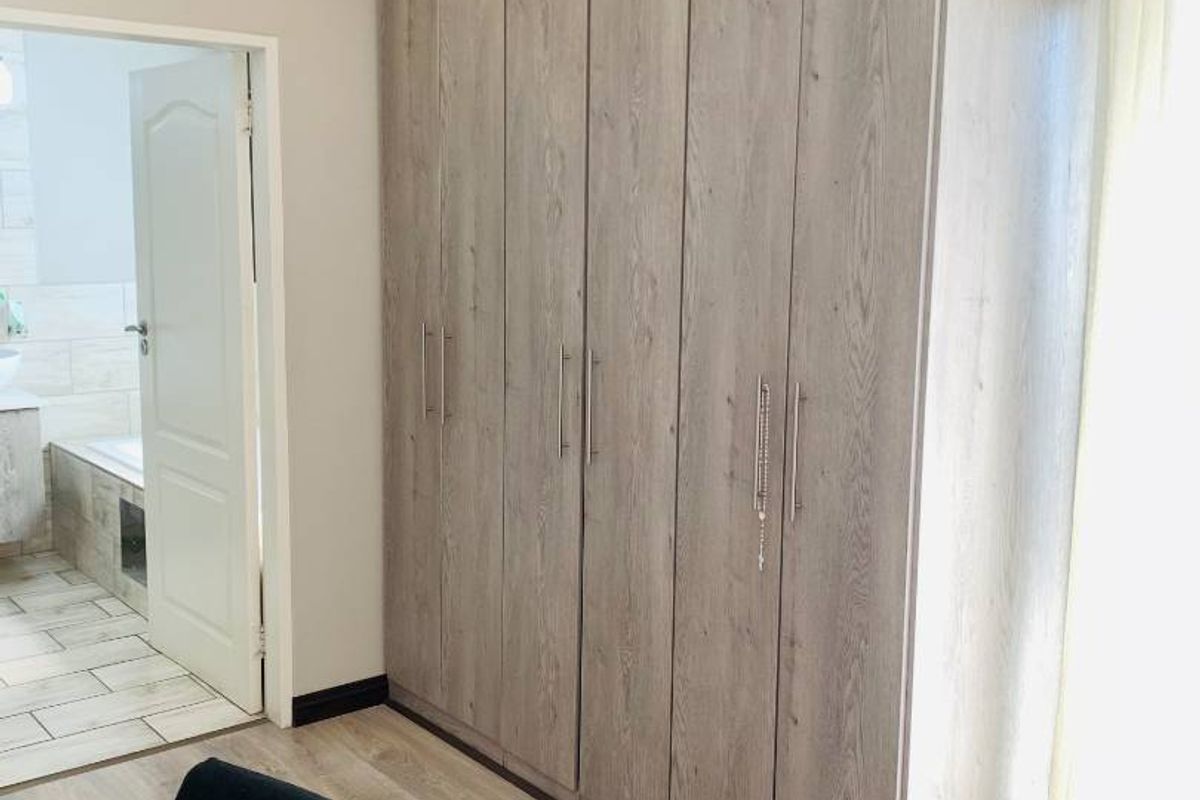 A well-maintained bedroom featuring modern wood-look built-in cupboards, light laminate flooring, and recessed ceiling lighting, with an adjacent en-suite bathroom.