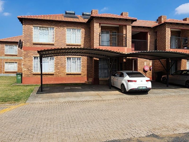 Front elevation of a face brick apartment complex featuring covered carports, tiled roofing, and upper-level balconies.