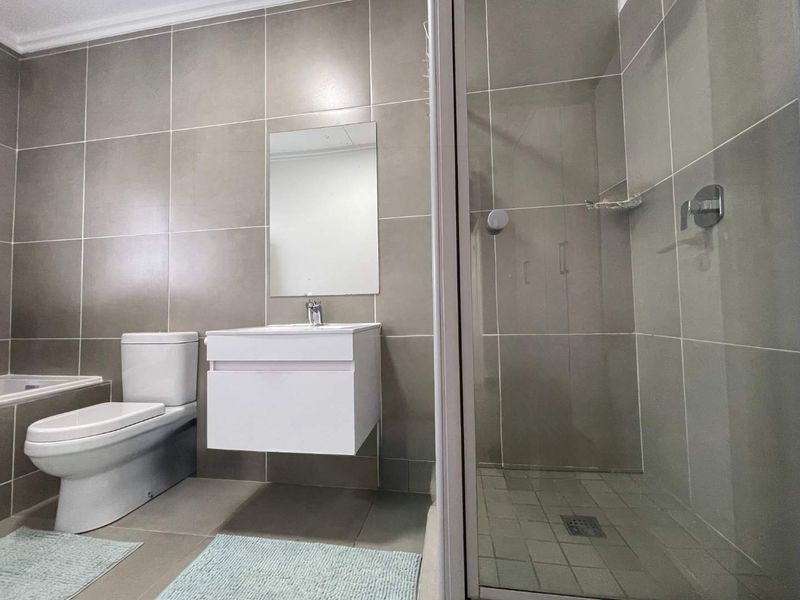 A modern, neutral-toned bathroom featuring a wall-mounted vanity, a glass-enclosed shower, and a toilet, finished with large-format wall and floor tiles.