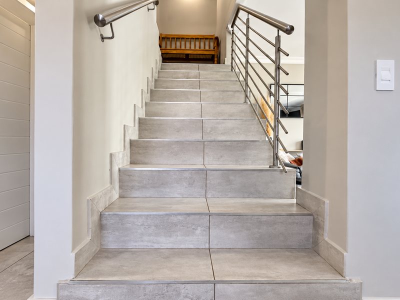 A modern staircase featuring large-format light grey tiles, stainless steel handrails, and a sleek balustrade, connecting the levels of the townhouse.