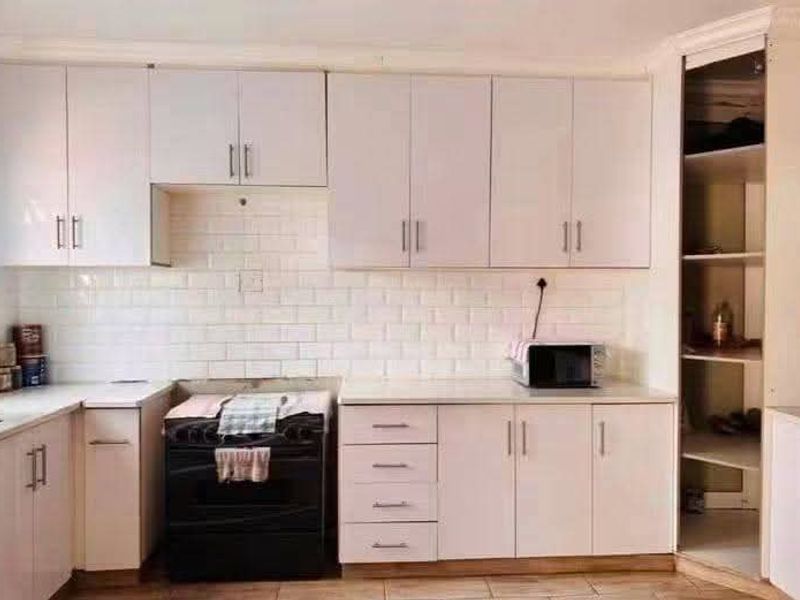 A functional kitchen featuring white cabinetry, a subway tile backsplash, and a built-in pantry, providing ample storage and workspace.
