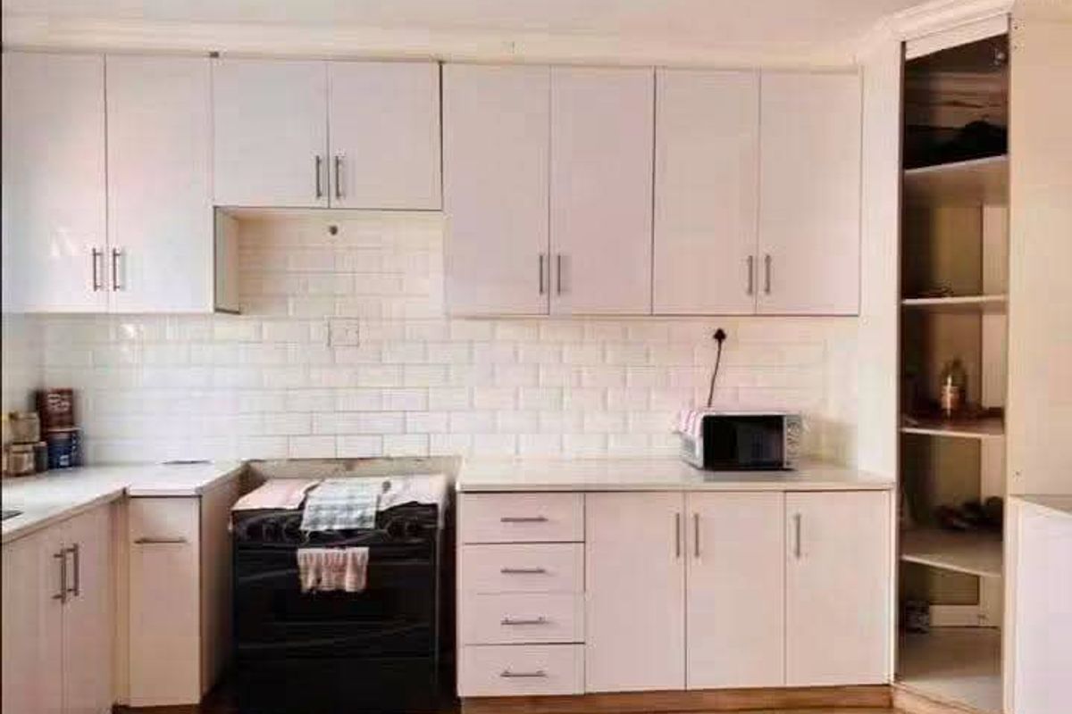 A functional kitchen featuring white cabinetry, a subway tile backsplash, and a built-in pantry, providing ample storage and workspace.