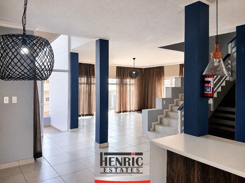 Spacious open-plan living area featuring tiled floors, a central staircase, and modern structural columns, offering a versatile layout for various living arrangements.