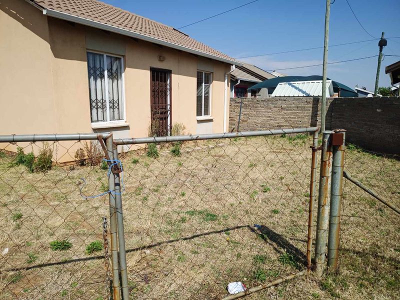 Rear exterior view of the property featuring a chain-link fence, metal gate, and a small yard area with a brick boundary wall.