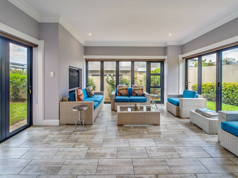 Bright and spacious living room featuring large aluminium sliding doors, tiled flooring, and a built-in fireplace, offering seamless access to the garden.