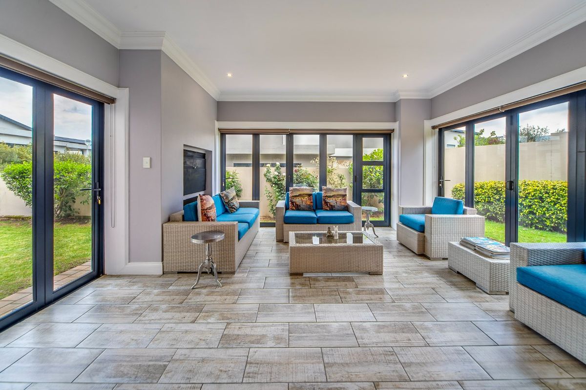 Bright and spacious living room featuring large aluminium sliding doors, tiled flooring, and a built-in fireplace, offering seamless access to the garden.