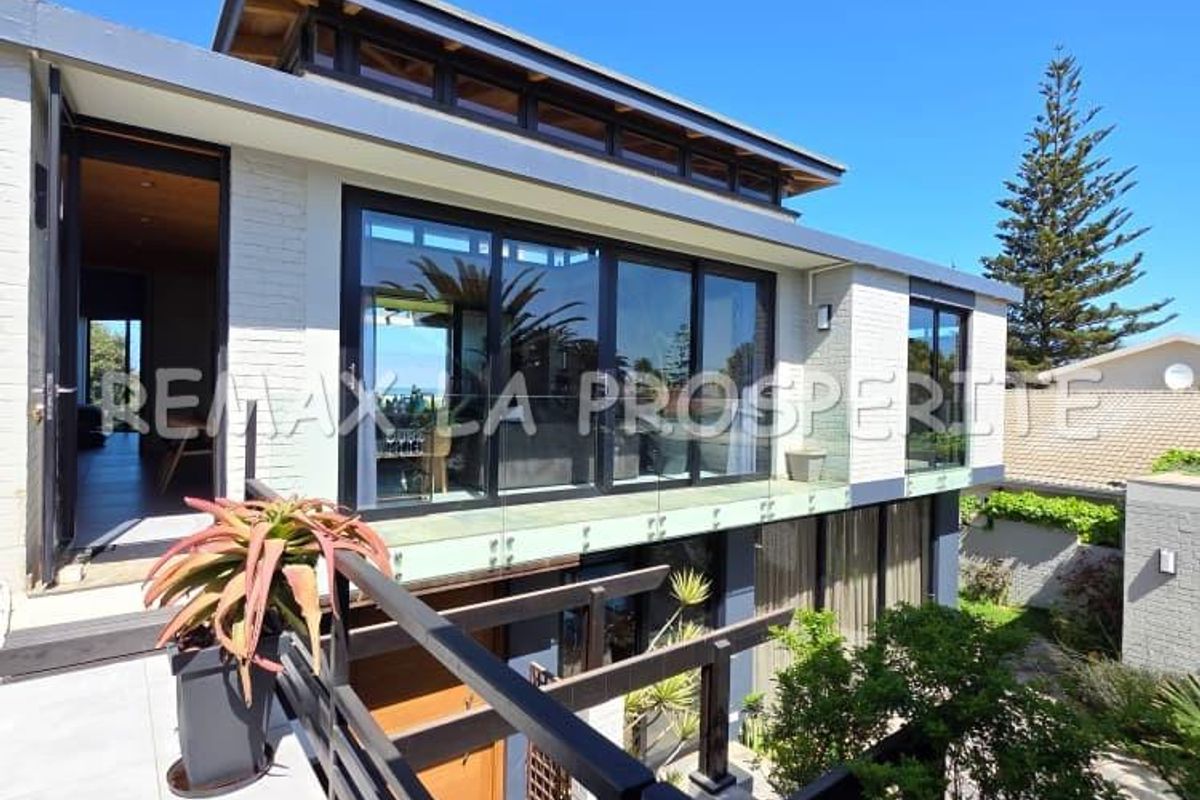 Modern rear exterior view featuring a spacious tiled balcony with glass balustrades, large sliding doors, and contemporary architectural design.