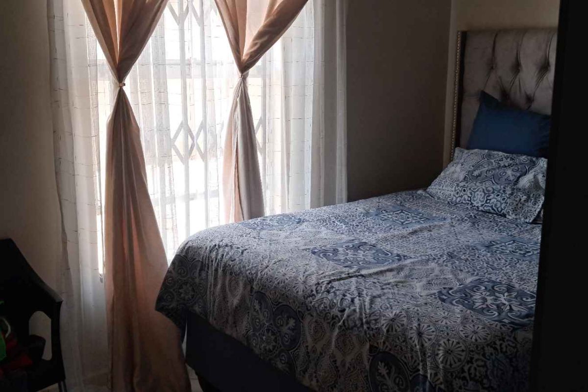A bedroom featuring a window with security bars and sheer curtains, providing natural light to the space.