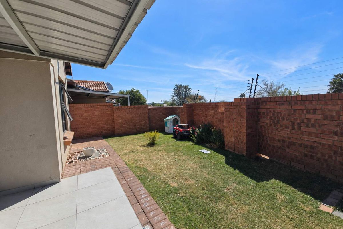 A private rear garden featuring a tiled covered patio, brick boundary walls, and electric security fencing.