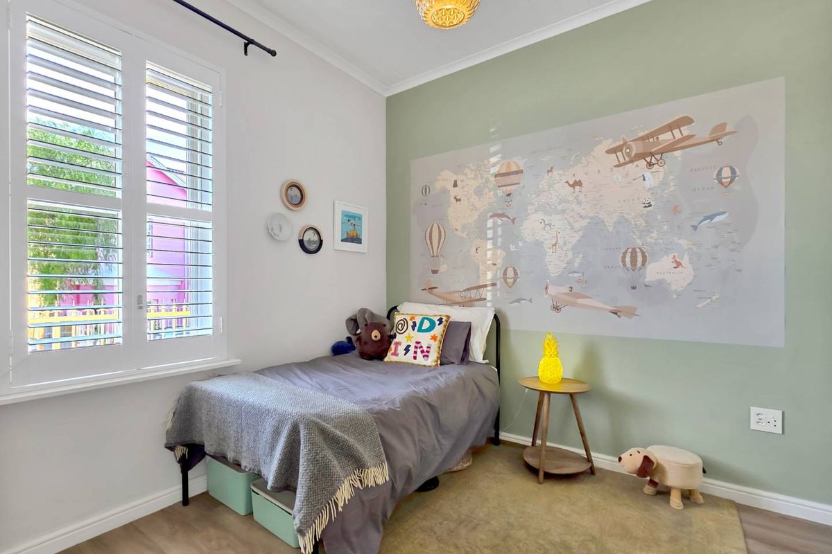 A bright and well-maintained bedroom featuring plantation shutters, timber-look flooring, and a feature wall with a decorative mural.