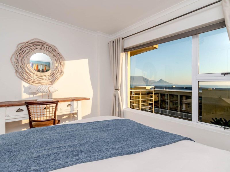 A bright bedroom featuring a large window with scenic mountain and sea views, providing ample natural light and a pleasant atmosphere.