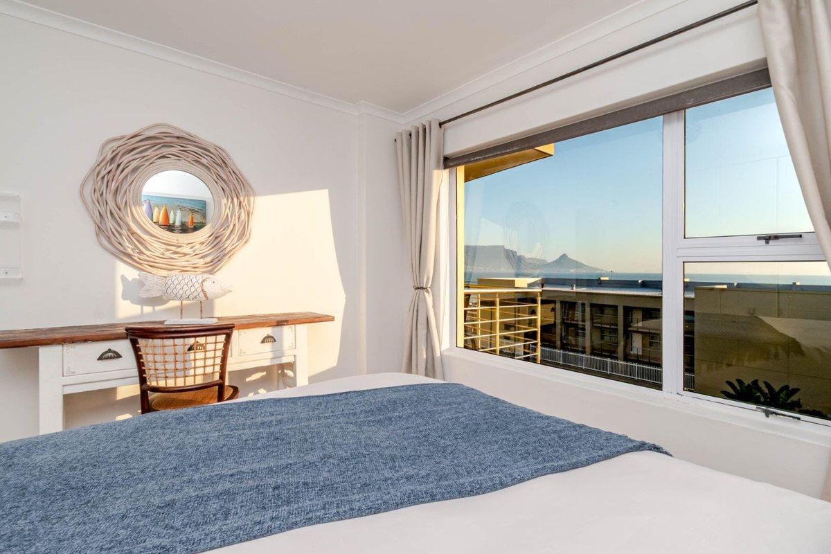 A bright bedroom featuring a large window with scenic mountain and sea views, providing ample natural light and a pleasant atmosphere.