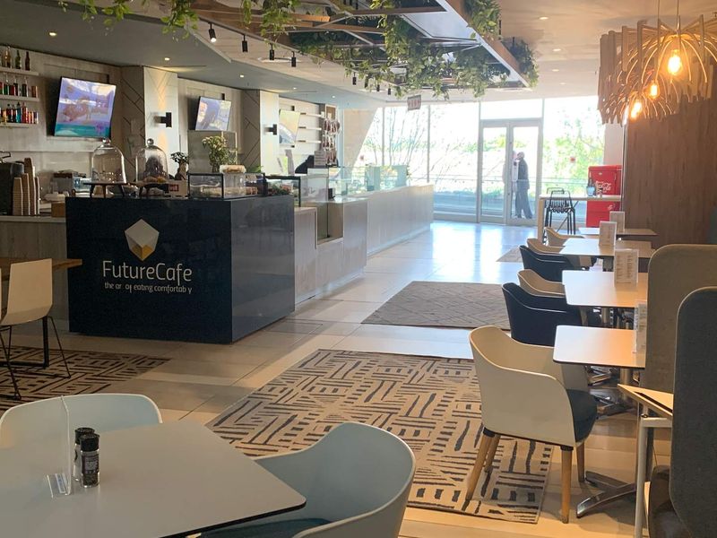 Modern open-plan cafe space featuring a central service counter, contemporary lighting, and large glass windows providing ample natural light.