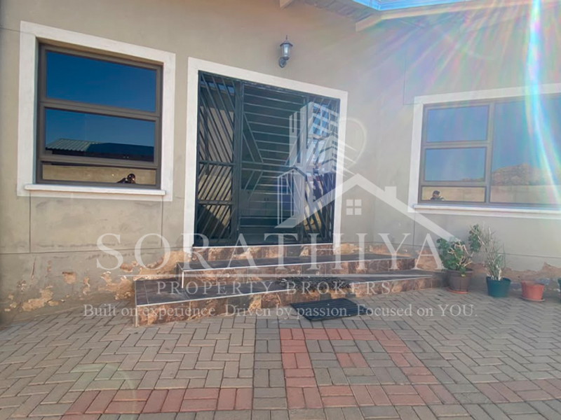 Rear exterior view of the property featuring a paved patio area, security gate, and aluminium window frames, showing signs of exterior wall wear.