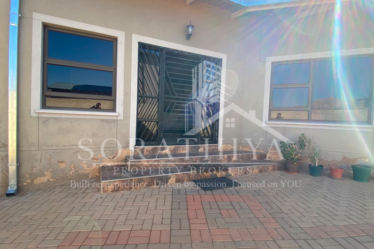 Rear exterior view of the property featuring a paved patio area, security gate, and aluminium window frames, showing signs of exterior wall wear.