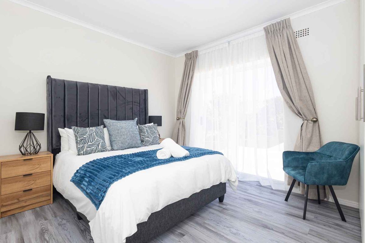 A well-maintained bedroom featuring modern laminate flooring, neutral walls, and a sliding glass door providing natural light and access to the exterior.
