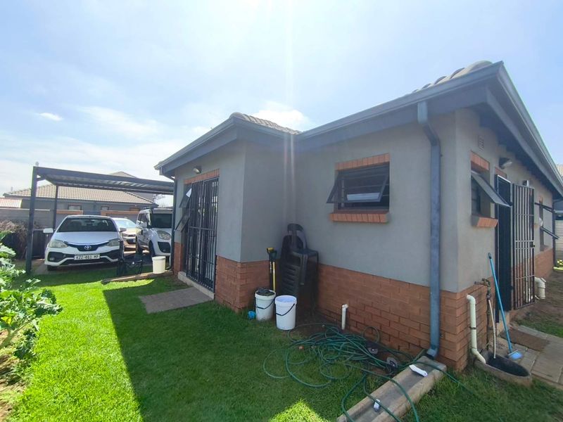 Rear view of the property featuring a brick and plastered facade, security gates, awning windows, and an attached carport area.