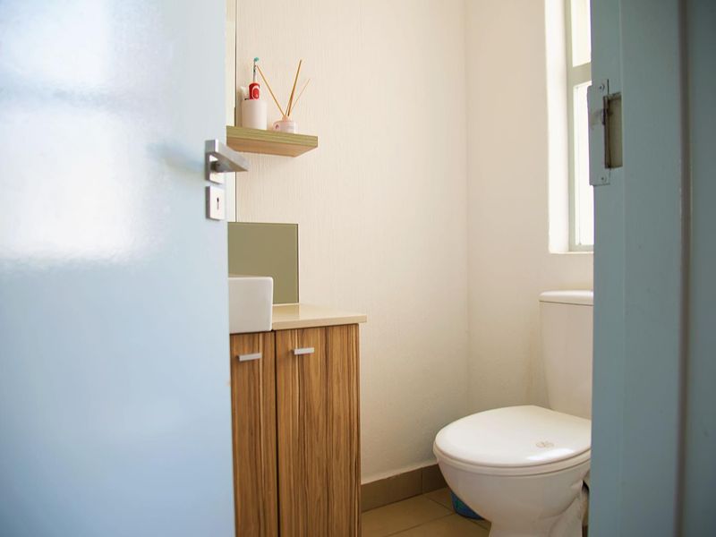 A compact bathroom featuring a wood-finish vanity cabinet with a vessel sink, a standard toilet, and a wall-mounted shelf under a window.