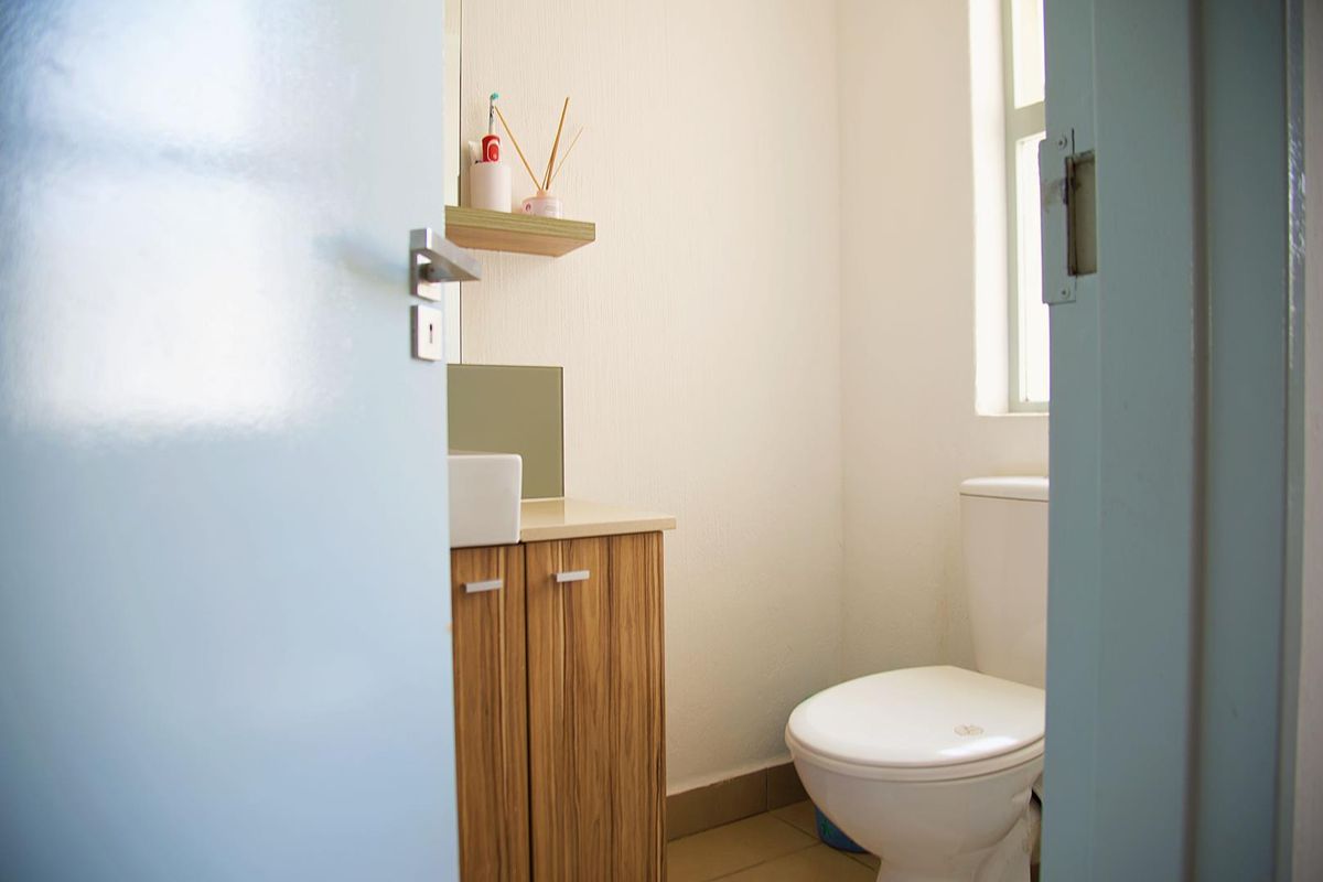 A compact bathroom featuring a wood-finish vanity cabinet with a vessel sink, a standard toilet, and a wall-mounted shelf under a window.