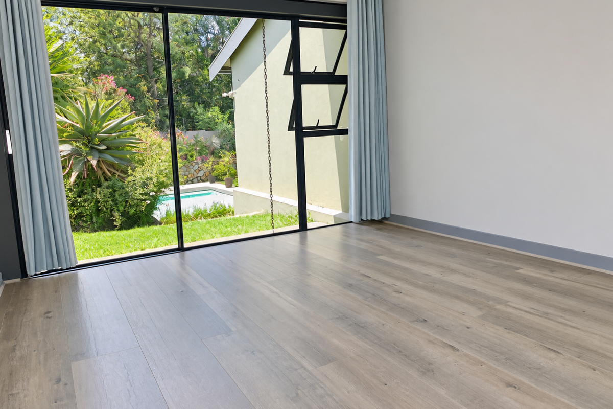 A bright, empty bedroom featuring modern laminate flooring and large sliding glass doors that open to a garden and pool area.
