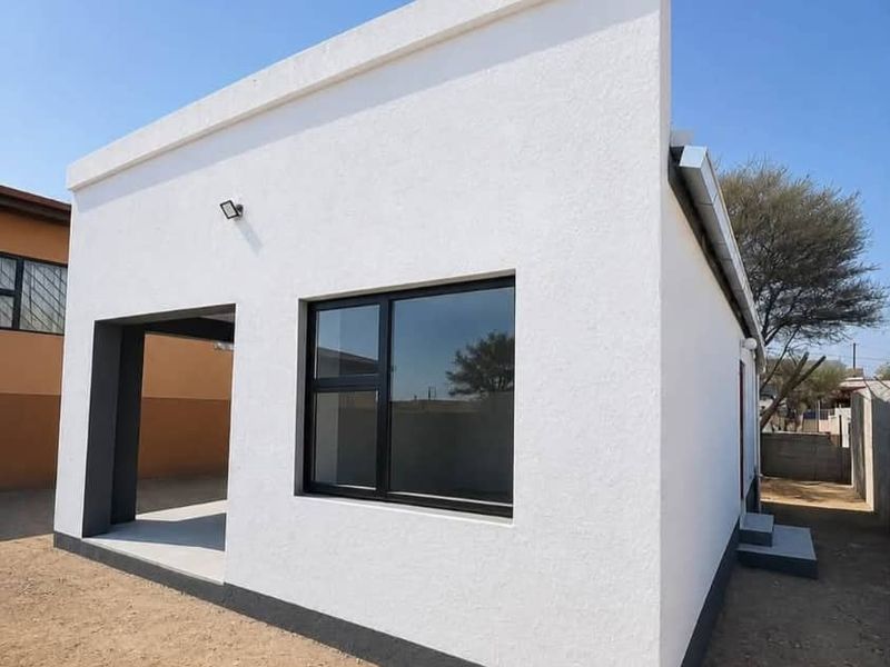 A modern, freshly painted exterior facade featuring clean white plaster, dark grey trim, and contemporary aluminium window frames.