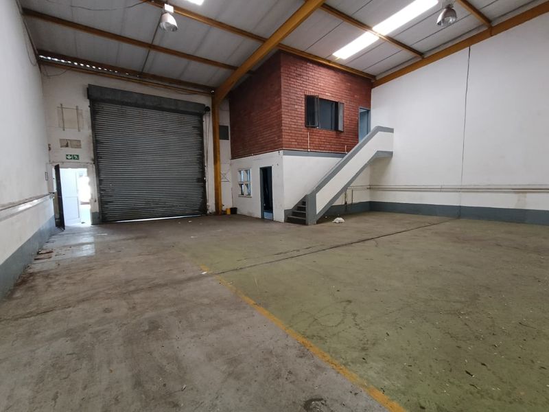 Spacious industrial warehouse unit featuring a high roller shutter door, concrete flooring, and a mezzanine level with an integrated staircase.