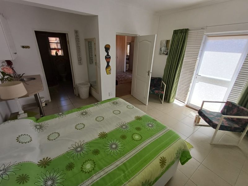 A bedroom featuring tiled flooring, a sliding glass door with blinds, and an integrated sink area, providing direct access to an adjoining room.
