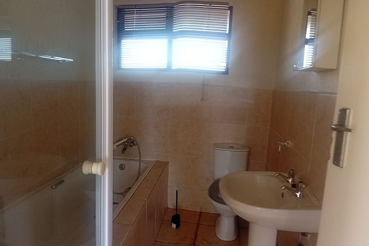 A functional bathroom featuring a bathtub with shower attachment, pedestal basin, toilet, and neutral wall and floor tiling.