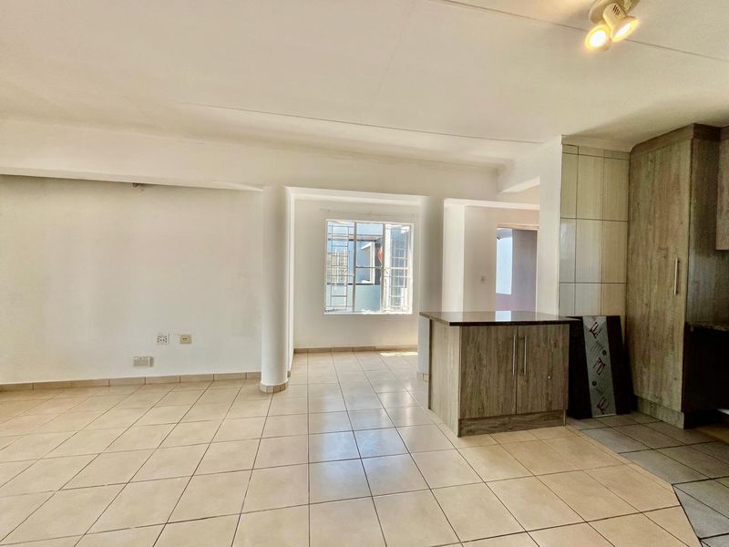 An open-plan living and kitchen area featuring tiled flooring, structural columns, and built-in cabinetry with an island, currently in a vacant, unfinished state.