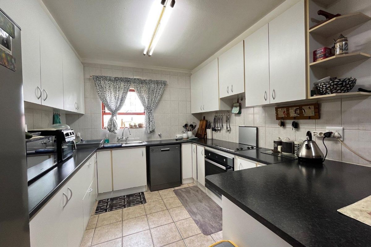 Functional kitchen featuring white cabinetry, dark laminate countertops, tiled splashbacks, and integrated oven and hob.