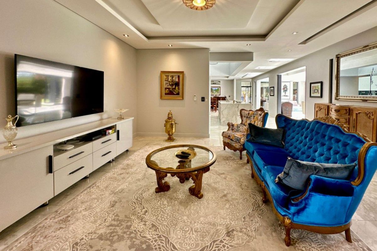 Spacious living room featuring a modern tray ceiling with recessed lighting and polished tile flooring, flowing into an open-plan kitchen area.