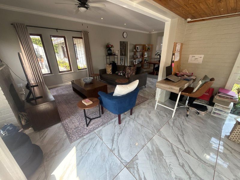 Spacious open-plan living area featuring large marble-look floor tiles, recessed lighting, a ceiling fan, and a combination of painted and exposed brick walls.
