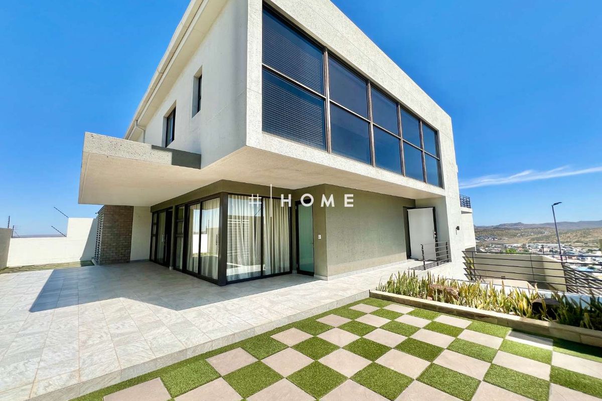 Modern two-story residence featuring a spacious tiled patio, large glass windows, and a landscaped checkerboard garden area with scenic views.