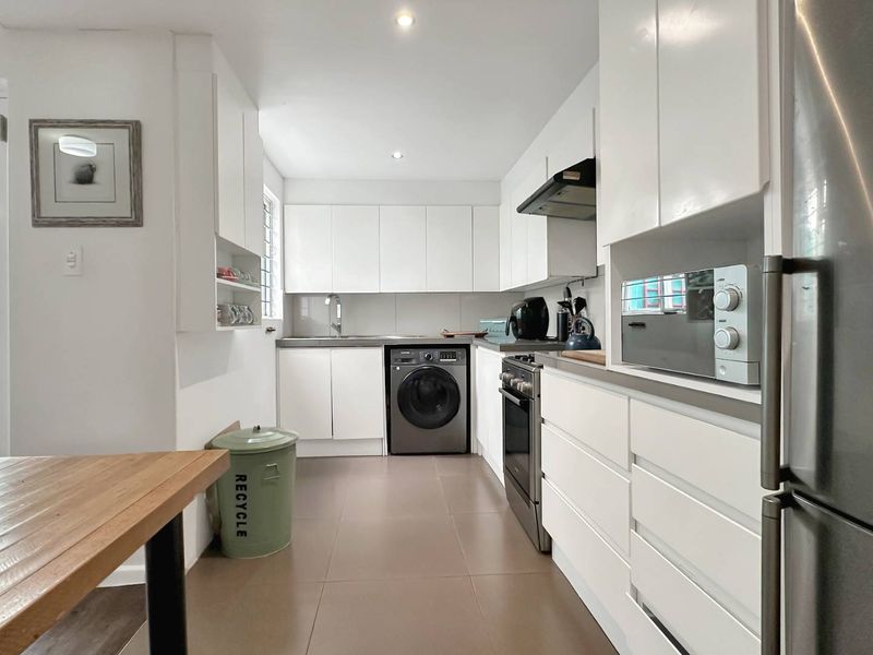A clean, modern kitchen featuring white cabinetry, tiled flooring, integrated appliances, and a functional layout with ample storage space.