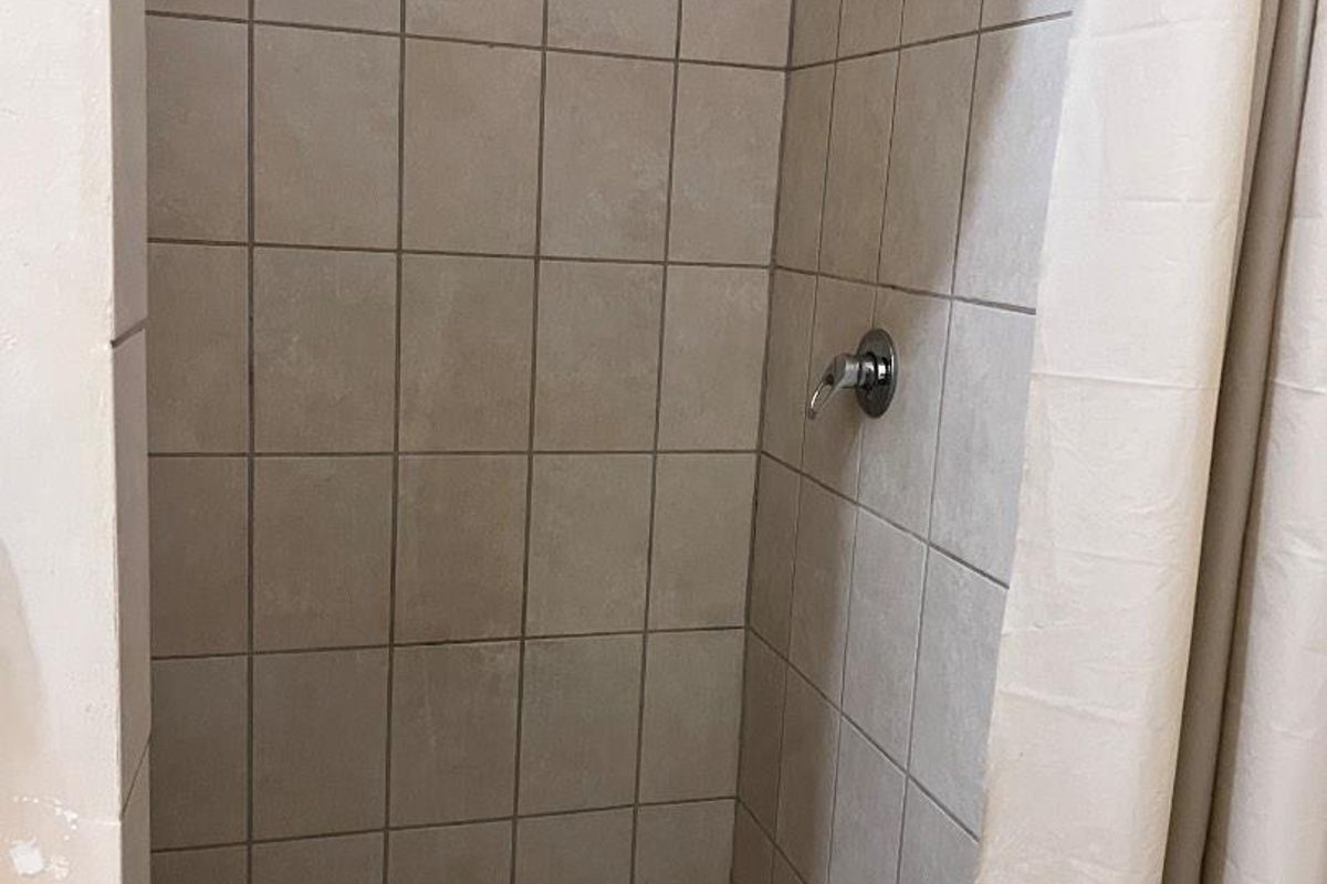 A compact shower stall featuring tiled walls and flooring with a built-in shower head and mixer tap.