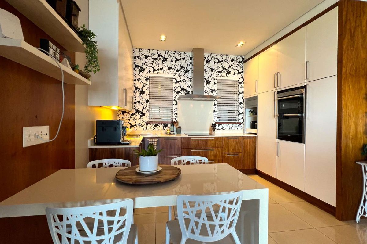 Modern kitchen featuring sleek white and wood-grain cabinetry, integrated oven, extractor fan, and stylish patterned backsplash with a functional dining area.
