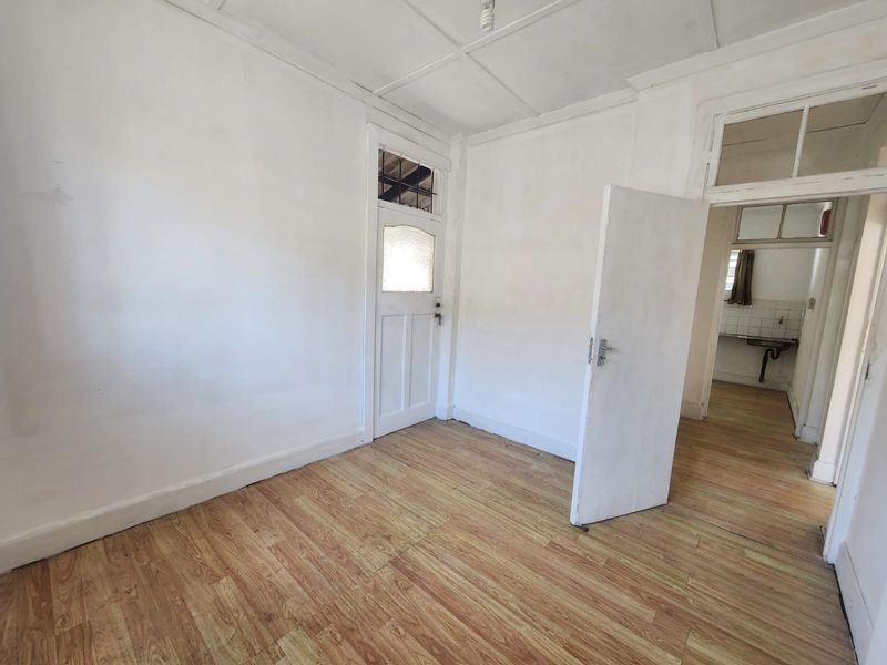 An empty living area featuring laminate flooring and a classic timber door with a glass insert, leading through to an adjacent utility space.