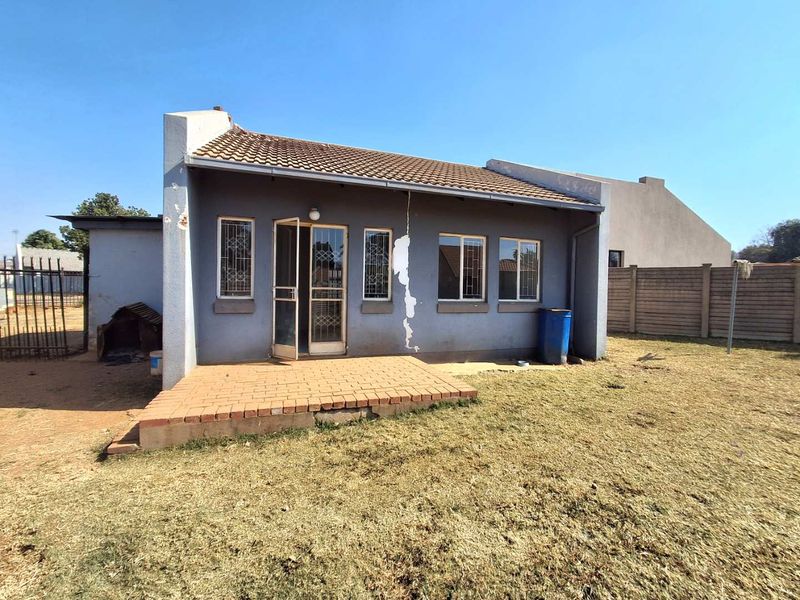 Rear view of the house featuring a brick patio, security gates, and a tiled roof, set within a fenced yard with visible exterior wall damage.