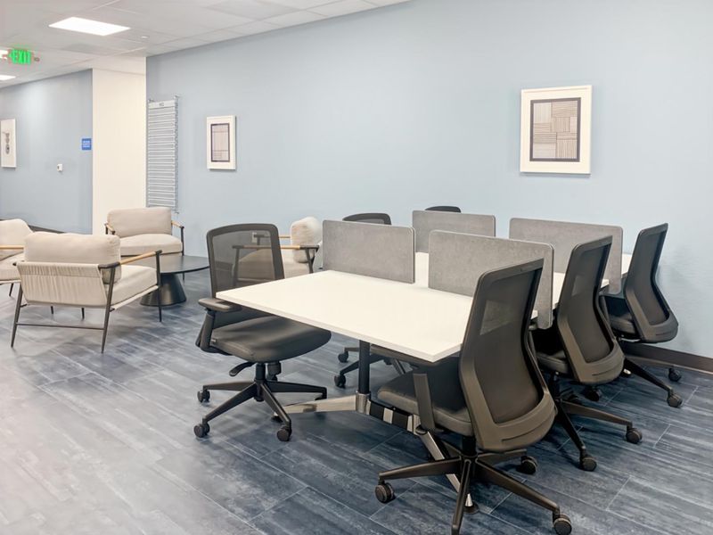 A modern office workspace featuring wood-look tile flooring, suspended ceiling with recessed lighting, and a professional open-plan layout.