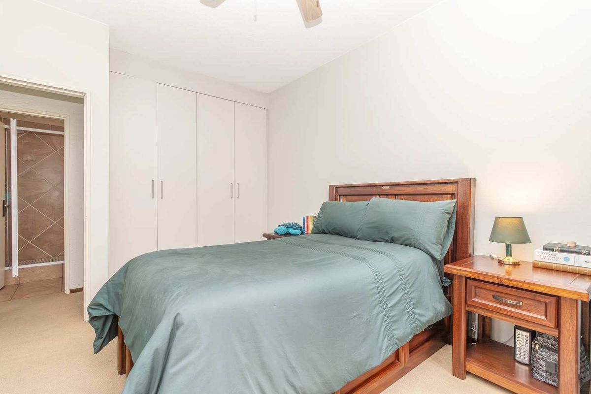 A bedroom featuring built-in cupboards and carpeted flooring, with an adjacent en-suite bathroom visible through the doorway.