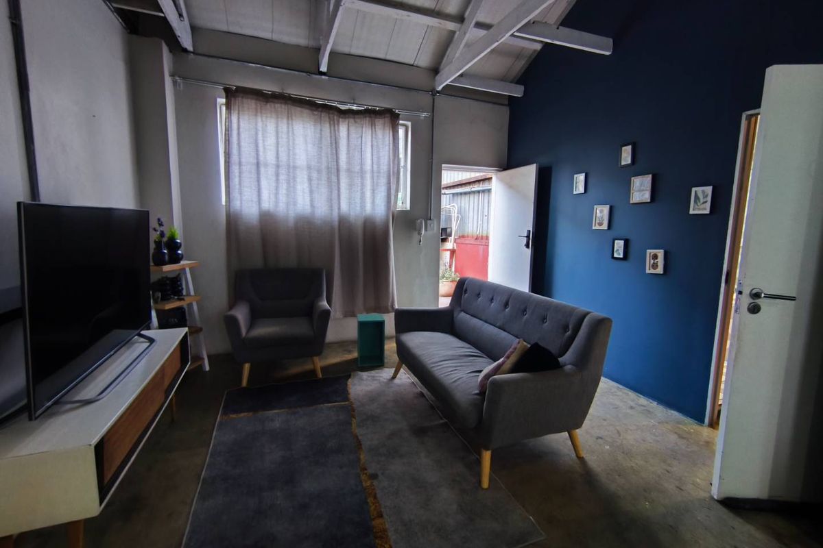 Living room featuring exposed timber ceiling beams, polished concrete flooring, and a bold blue accent wall with direct access to an outdoor area.