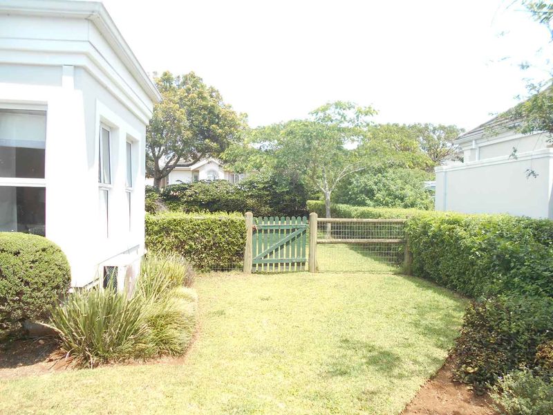 A private rear garden area featuring a well-maintained lawn, established hedging, and a timber gate providing access to the perimeter.