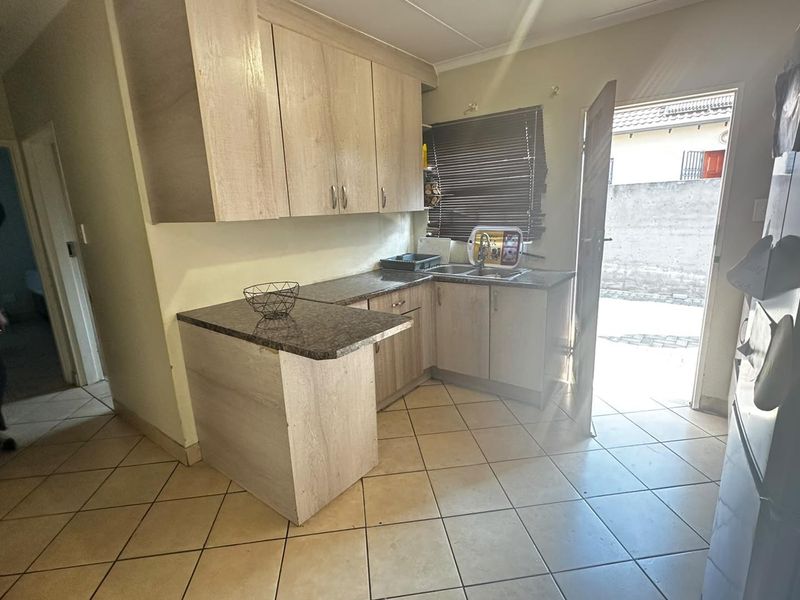 Compact kitchen featuring light wood-look cabinetry, granite countertops, and tiled flooring with direct access to the exterior.