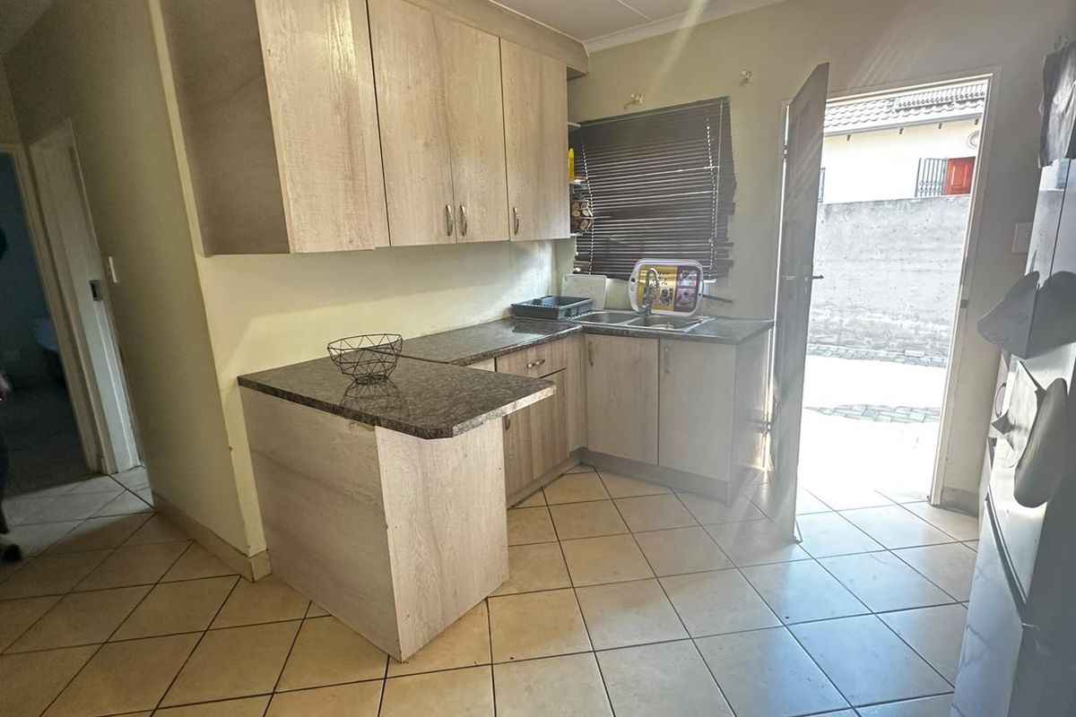 Compact kitchen featuring light wood-look cabinetry, granite countertops, and tiled flooring with direct access to the exterior.