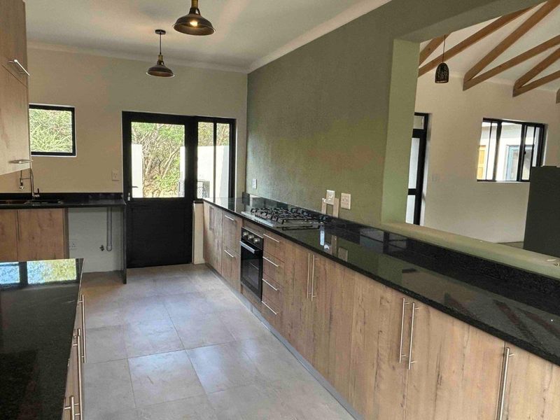Modern kitchen featuring wood-finish cabinetry, black granite countertops, a gas hob, built-in oven, and tiled flooring, with an open-plan layout.