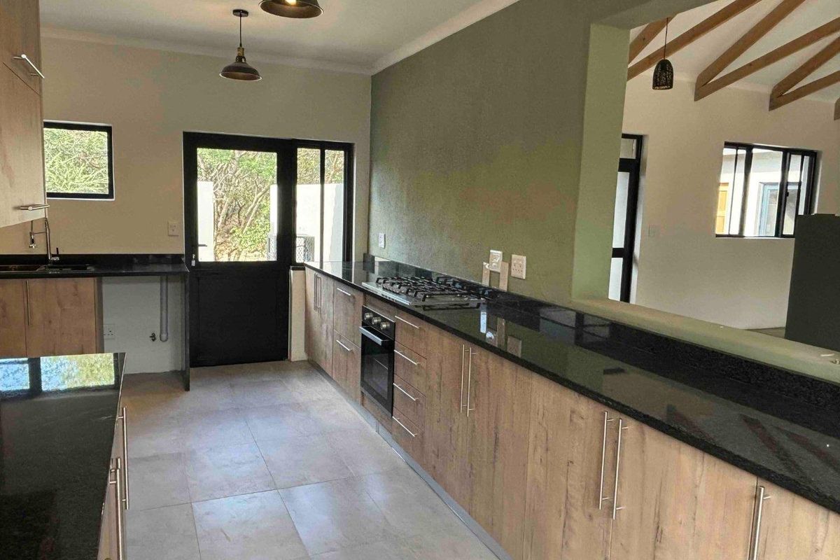 Modern kitchen featuring wood-finish cabinetry, black granite countertops, a gas hob, built-in oven, and tiled flooring, with an open-plan layout.
