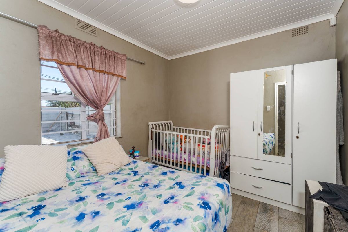A functional bedroom featuring tiled flooring, a white tongue-and-groove ceiling, and a window with security bars.